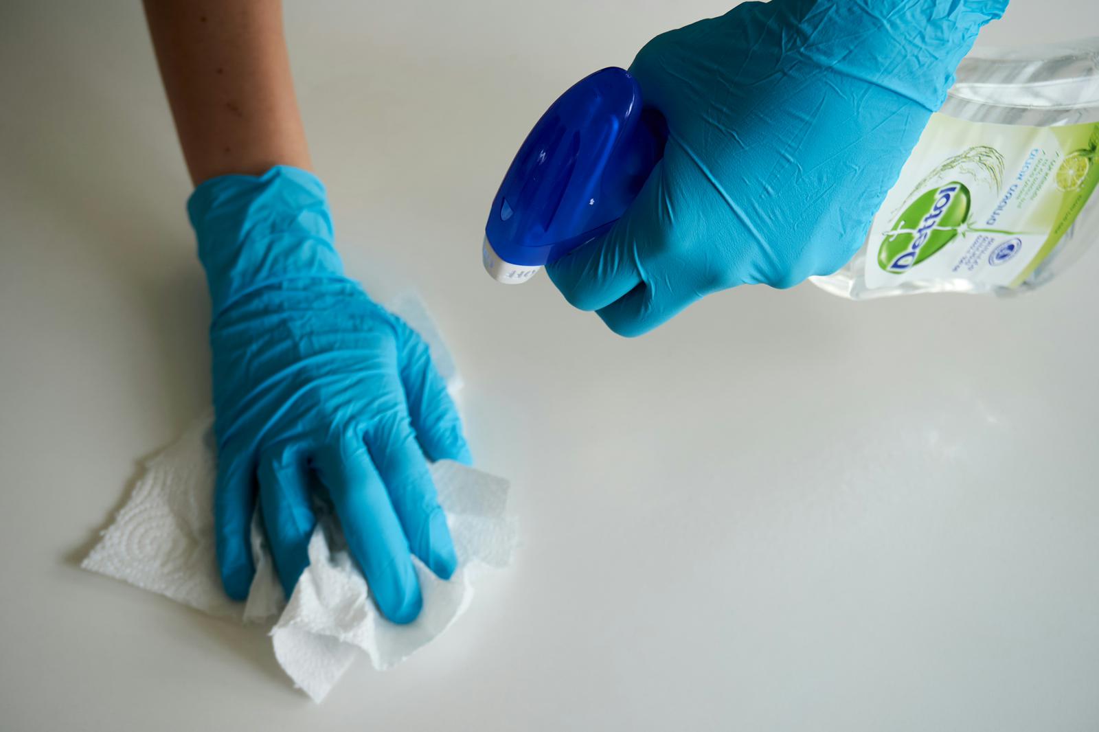 Hands in blue gloves spraying Dettol on a bathroom surface